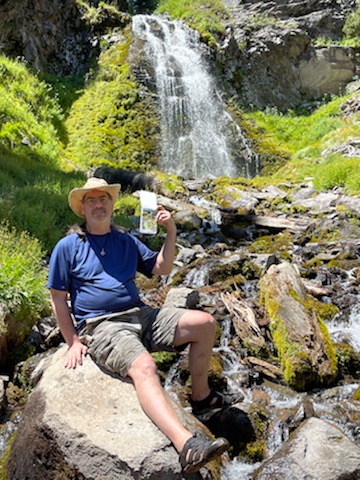  A man holding up a small sketchbook with a plein air painting in it at Plaikni Falls Oregon